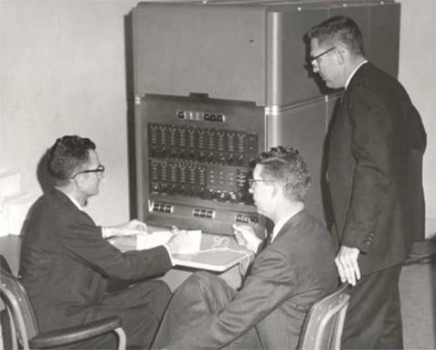 Dr. Thomas Tramel, far left, seated at the console of MSU's first computer and joined by other MSU colleagues. Photo courtesy of the Mitchell Memorial Library University Archives Digital Collection.